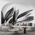 Black and white botanical leaf mural wallpaper styled in a modern living room with minimal furniture and natural light