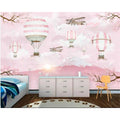 Hot air balloon wallpaper creating a magical atmosphere in a bright nursery with pink accents and white furniture