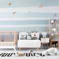 Blue and white striped nursery wallpaper with gold planes in a bright modern nursery with white furniture